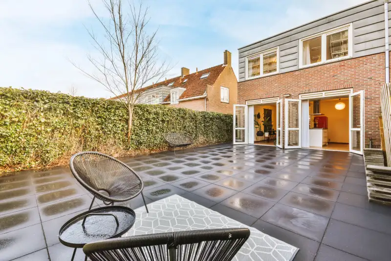Strak bestraatte achtertuin met antraciet tegels en groene haag