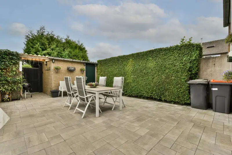 Onderhouden achtertuin met schone tegels, tuinset en strak gesnoeide haag